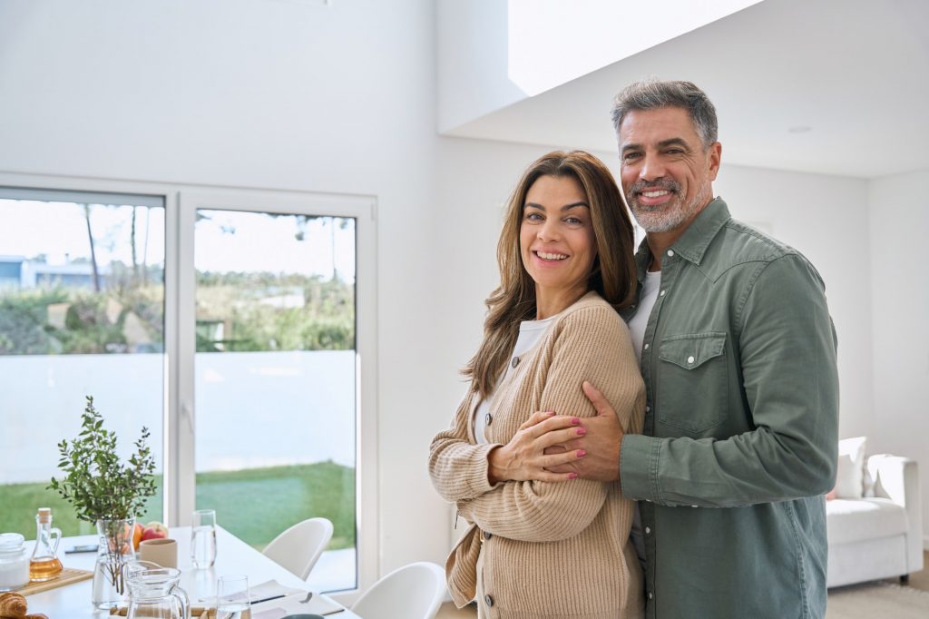 Portrait of happy smiling mature couple real estate owners standing at home.